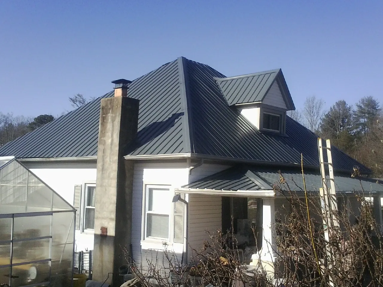 Dark blue standing seam metal roof on a white farmhouse with dormer — Slate & Tile Roof Repair by Roofing Brothers in Bloomington
