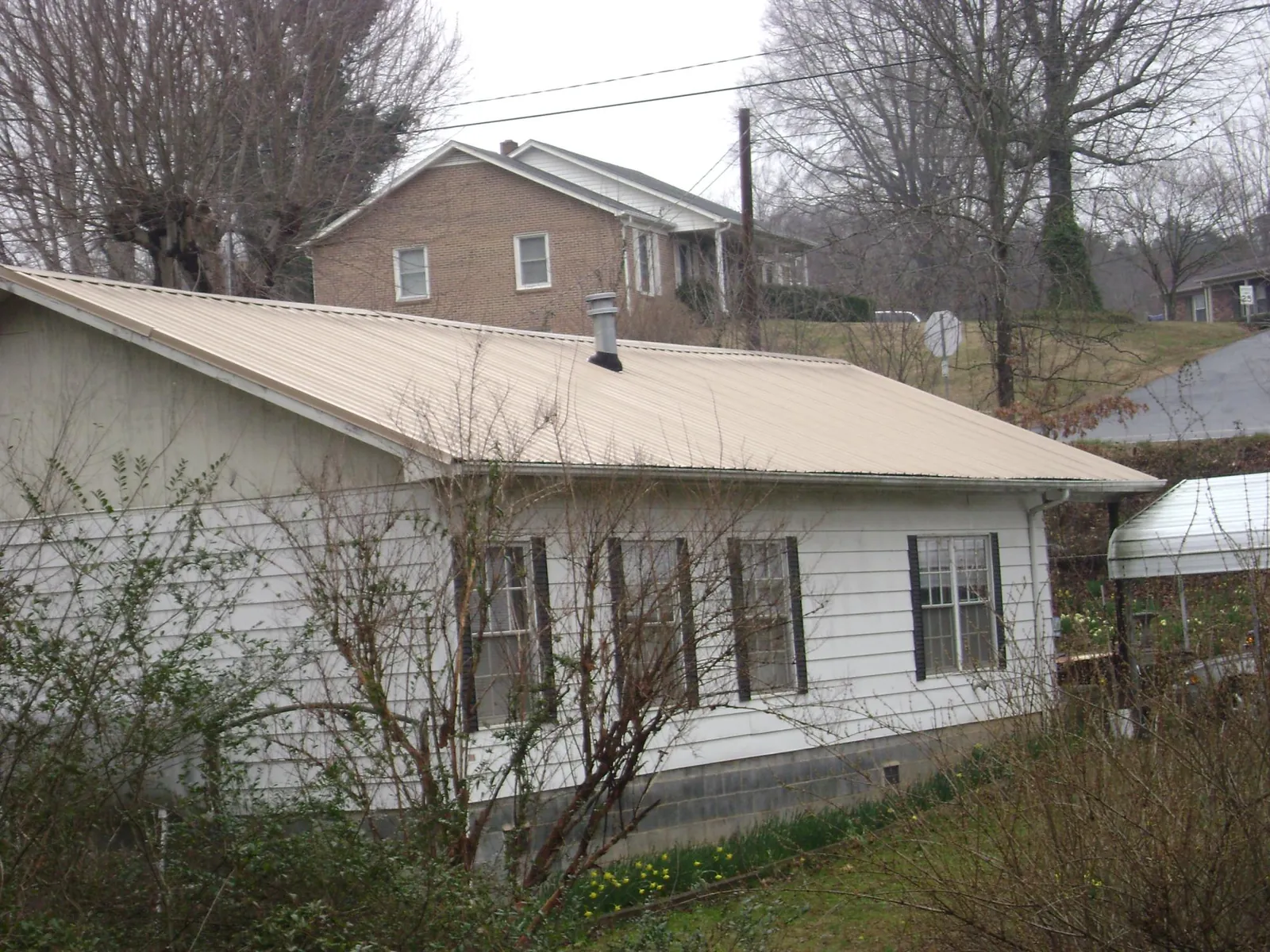 Tan metal roof on a white sided house set into a hillside — Commercial Roofing by Roofing Brothers in Bloomington